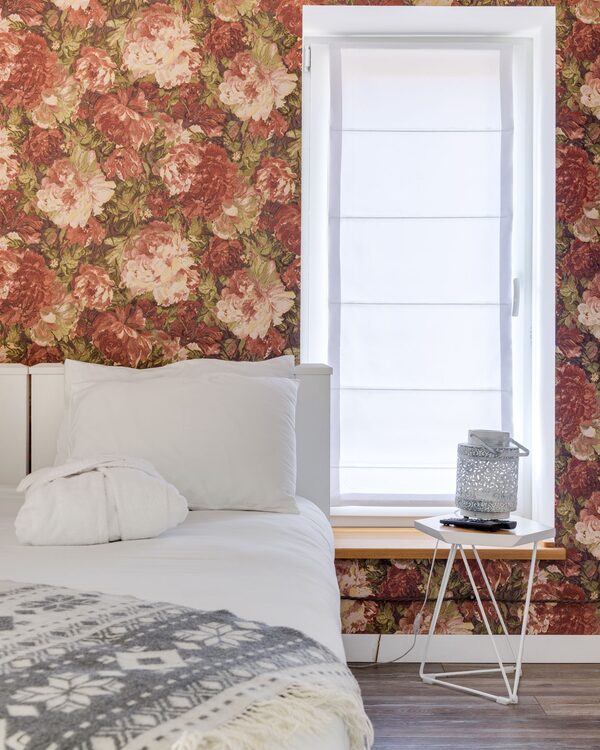 Bedroom with a warm red rose floral wallpaper beside a bright window