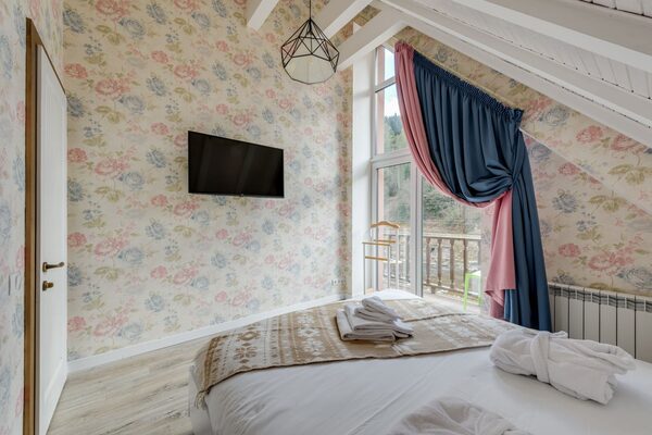 Bedroom with a soft floral wallpaper, exposed ceiling beam and a draped window