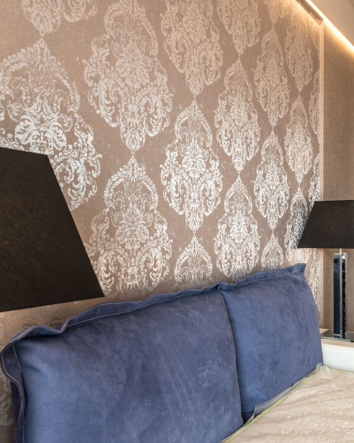 Elegant bedroom with a champagne damask wallpaper feature wall behind an upholstered headboard