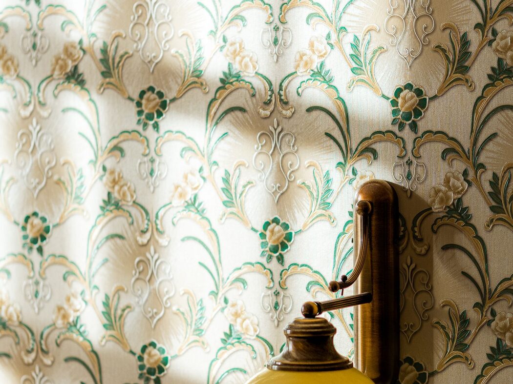 Detail of a green botanical wallpaper wall lit by a brass wall sconce