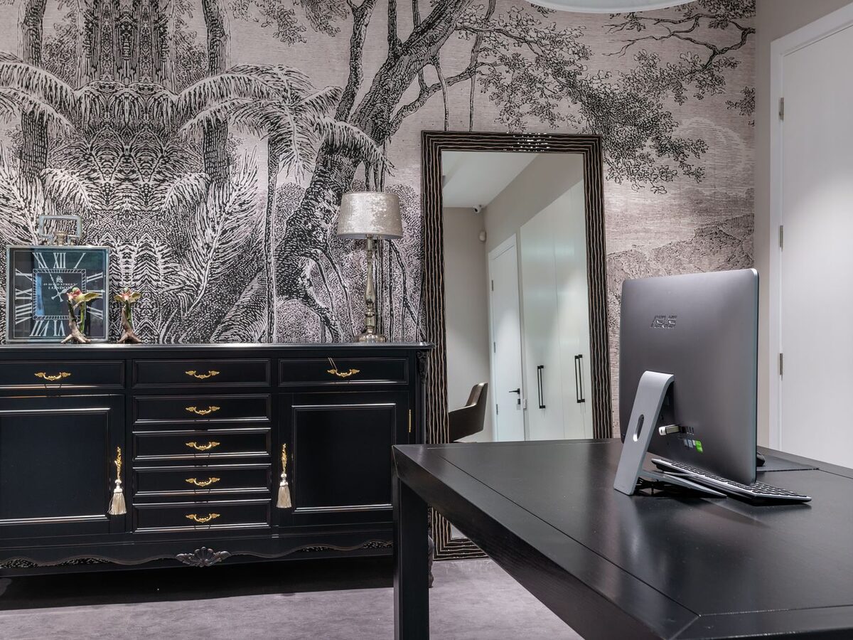 Home office with a dramatic dark jungle mural wallpaper behind a black cabinet and desk